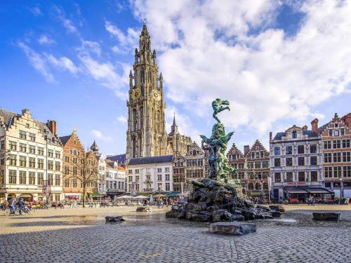 einem Stadtplatz mit einer Statue vor einem Uhrturm in der Unterkunft Novotel Antwerpen in Antwerpen