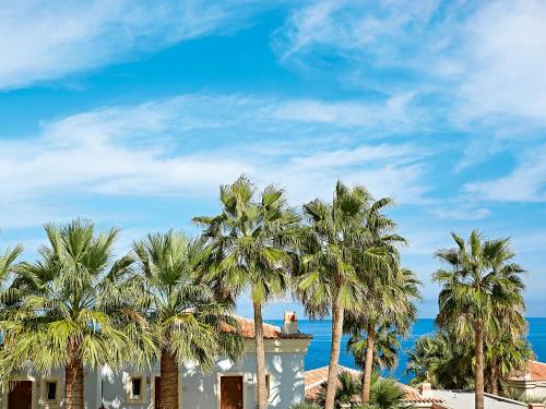 a building with palm trees in front of the ocean at Grecotel Marine Palace & Aqua Park in Panormos Rethymno