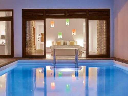 a pool with a chair and a bed in a room at Amirandes, A Grecotel Resort to Live in Gouves