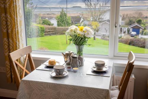 un tavolo con un vaso di fiori su un tavolo con una finestra di Summerfield Lodge Garden Cottage a Youghal