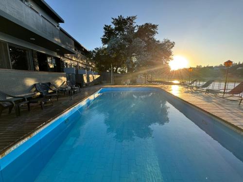 a swimming pool with the sun setting behind a building at Nuevo Hotel Ciervo de Oro- By HVH in Villa Carlos Paz