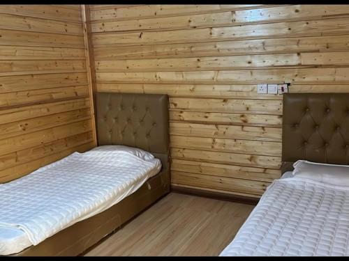 two beds in a room with wooden walls at الكوخ الريفي in Al Majma'ah