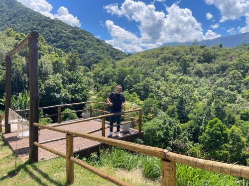 un hombre parado en una plataforma de madera en las montañas en Casa para temporada em meio à natureza., en Cachoeiras de Macacu