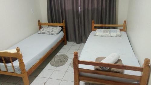 two twin beds in a room with a window at Apto 03 - 1 quarto com 2 camas solteiro e garagem, possui ventilador de teto in Cascavel