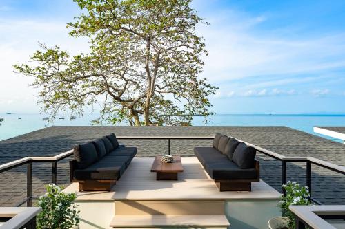 a balcony with two couches and a table and the ocean at Kove Samui - Absolute Beachfront Villas in Koh Samui 