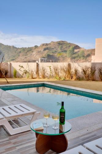 a table with two glasses of wine next to a swimming pool at ELIVAAS Shourya Bliss Lux 3BHK Villa with Pvt Pool, Udaipur in Udaipur