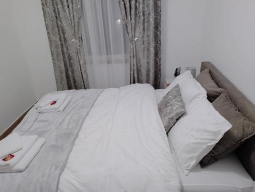 a bed with white sheets and pillows next to a window at Apartman Dve lipe in Palić