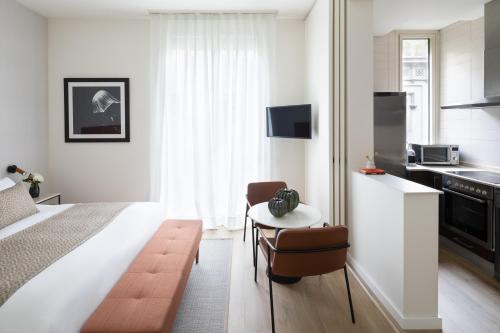 a bedroom with a bed and a small table and a kitchen at Murmuri Residence Concepció in Barcelona