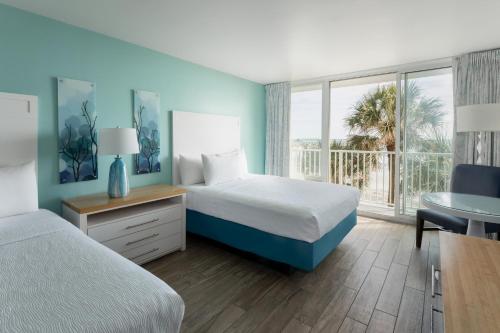 a hotel room with two beds and a desk and a window at Tides Folly Beach in Folly Beach