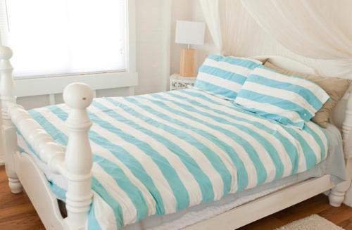 a white bed with a blue and white striped comforter at Barbuda Cottages in Codrington Village