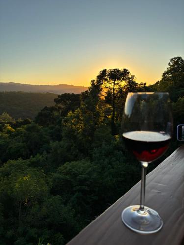 a glass of wine sitting on a ledge with the sunset at Reserva Linha Bonita in Gramado