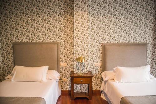 two beds sitting in a room with wallpaper at Hotel A Casa Do Rio in Padrón