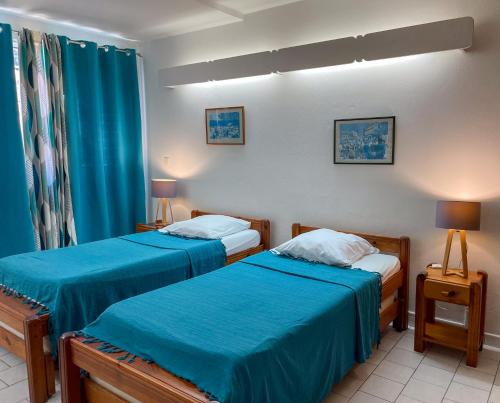 two beds in a hotel room with blue sheets at Salines Studios in Sainte-Anne