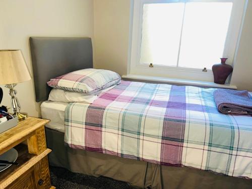 ein Schlafzimmer mit einem Bett mit einer karierten Decke und einem Fenster in der Unterkunft Single Room - Bed for the night - Close to Beach in St. Leonards