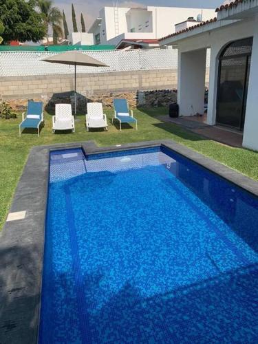 a large blue swimming pool with chairs and an umbrella at Casa en lomas de Cocoyoc in Texcalpan