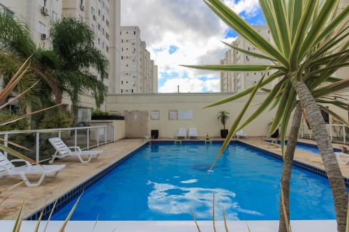 a large swimming pool with chairs and a palm tree at Ap Cloe com piscina próximo ao Aeroporto in Porto Alegre