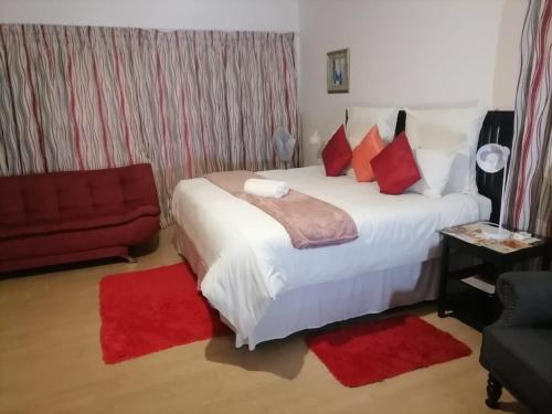 a bedroom with a bed with red pillows and a red couch at Ezamampondo Guest House in King Williamʼs Town