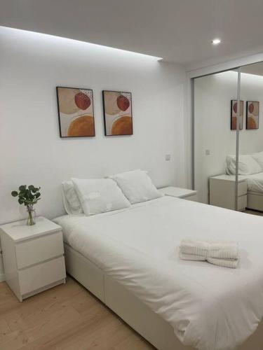 a white bedroom with a large bed and two pictures at Lovely 2 bedroom apartment in South Lisbon in Barreiro