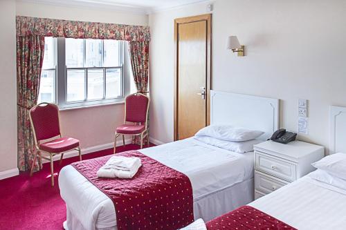 a bedroom with two beds and two chairs and a window at Afton Hotel in Eastbourne