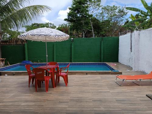 una mesa con sillas y una sombrilla junto a la piscina en Casa na ilha de Itaparica, en Itaparica