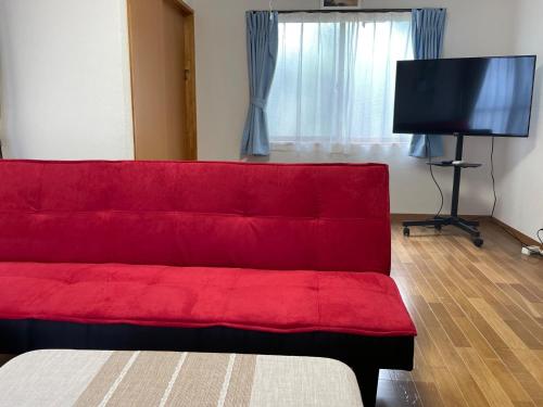ein rotes Sofa im Wohnzimmer mit einem Flachbild-TV in der Unterkunft Yoka House - Vacation STAY 46247v in Tokunoshima