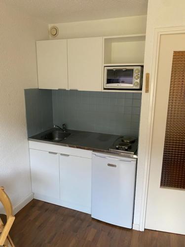 a small kitchen with white cabinets and a microwave at Appartement pied des pistes in Puy-Saint-Vincent