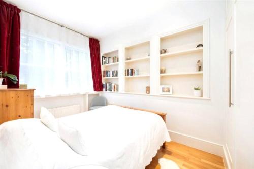 two beds in a white bedroom with a window at Neat, bright, and convenient. in London
