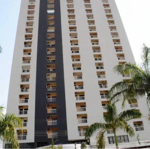 a tall building with palm trees in front of it at Flat confortável e econômico hotel condomínio cristal place in Goiânia