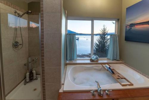 a bathroom with a tub and a shower and a window at Juneau Oceanfront Home Overlooking Auke Bay in Mendenhaven
