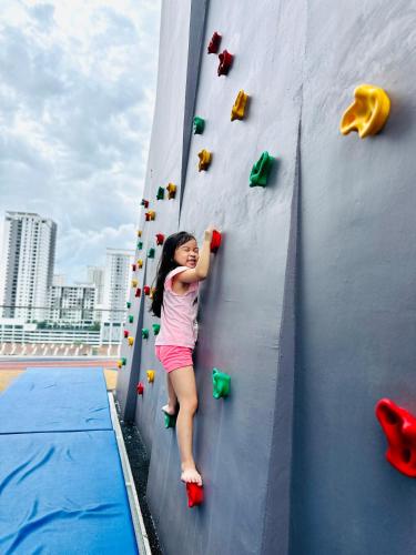 a young girl is climbing a climbing wall at New 2BR or 3BR Homey Getaway stay 7 to 10 pax at Urban Suites, Georgetown by URBAN STAYCATION LOD in Jelutong
