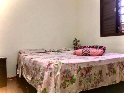 ein Schlafzimmer mit einem Bett mit einer rosa Blumendecke in der Unterkunft Quarto confortável lago igapó in Londrina