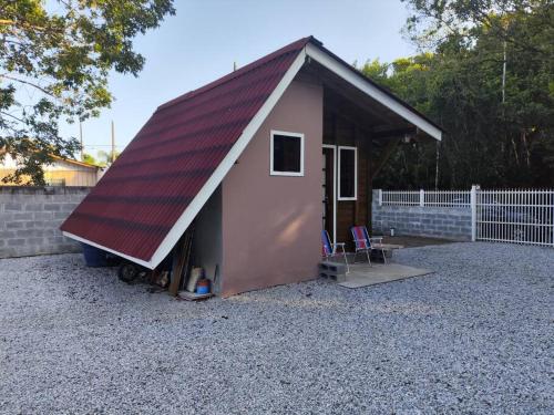un petit hangar avec un toit rouge sur gravier dans l'établissement Casa - Chalé da praia, à Pontal do Paraná