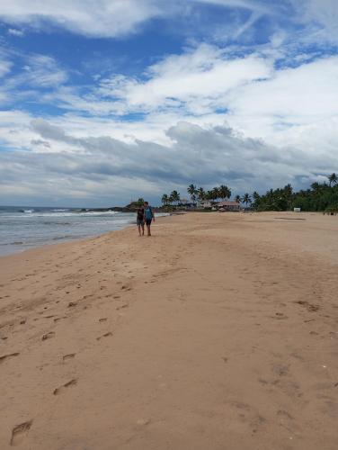 two people walking on a sandy beach near the ocean at Nade Villas Ahungalla in Ahungalla