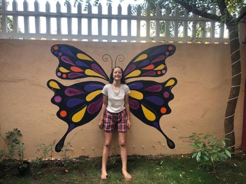a woman standing in front of a butterfly painted on a wall at Shree Hari Guest House in Anjuna