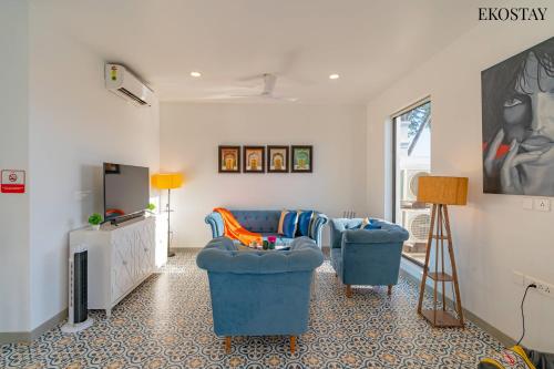 ein Wohnzimmer mit 2 blauen Stühlen und einem TV in der Unterkunft EKOSTAY Luxe - Jade Villa I Infinity Pool I Paddy Field Views in Candolim