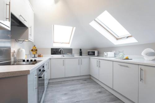 a white kitchen with white cabinets and skylights at Elliot Oliver - Modern 2 Bedroom Town Centre Apartment in Cheltenham