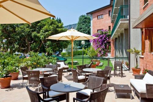 un patio extérieur avec des tables, des chaises et des parasols dans l'établissement Hotel Gabbiano - Garda Lake Collection, à Garde
