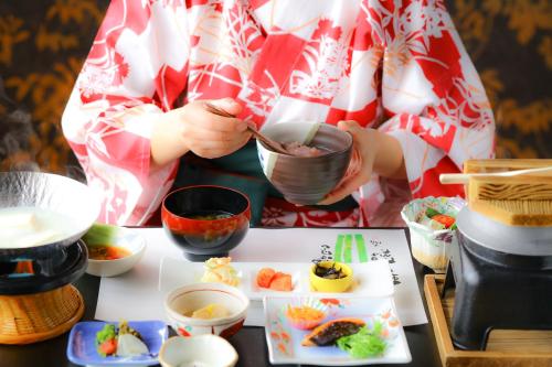 a woman is holding a bowl of food with chopsticks at 別所温泉 七草の湯 in Ueda