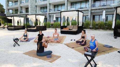 a group of women sitting in a yoga pose on the beach at The Beach Samui in Taling Ngam Beach