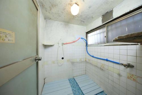 La salle de bains est pourvue d'une douche avec flexible bleu et rouge. dans l'établissement ドミトリー月の光莉, à Tokyo