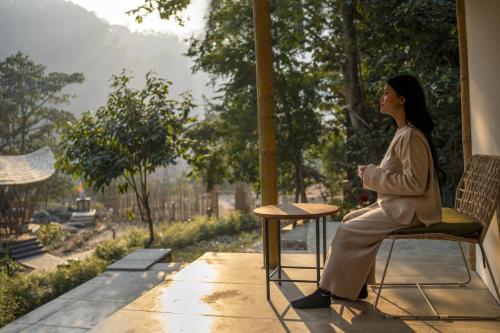 a woman sitting on a chair looking out a window at ONENESS Rishikesh by Ganga Kinare - A Luxury Wilderness Resort in Rishīkesh