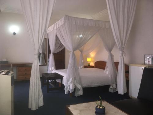 - une chambre avec un lit à baldaquin et des rideaux blancs dans l'établissement Ivotel, à Antananarivo