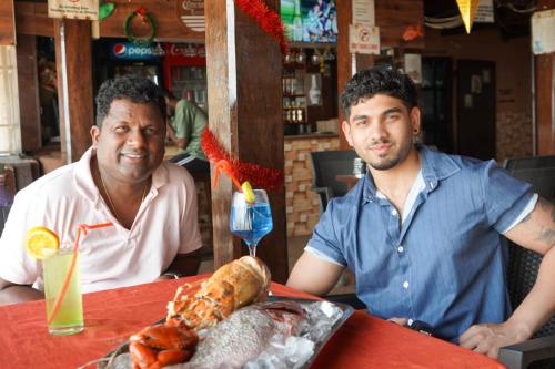 two men sitting at a table with a plate of food at Saritas Guest House - Bogmalo Beach in Bogmolo