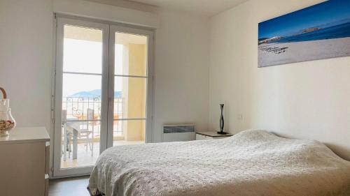 a white bedroom with a bed and a large window at Appartement Les Oliviers L'ILE ROUSSE in LʼÎle-Rousse