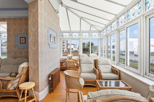 a conservatory with chairs and tables and windows at Marine Hotel in Paignton