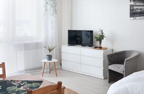 a white bedroom with a tv and a chair at Osiedle Zwycięstwa Chic Studio in Poznań