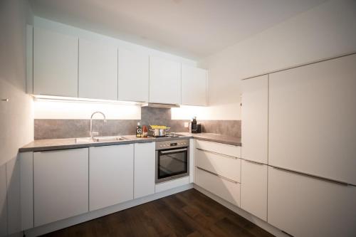 a white kitchen with white cabinets and a sink at Brentschpark 33 in Scuol