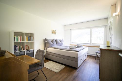1 dormitorio con cama, escritorio y ventana en Brentschpark 33, en Scuol