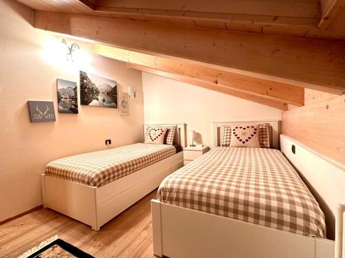 two beds in a room with wooden ceilings at Mansarda Le Genziane di Fiemme in Cavalese