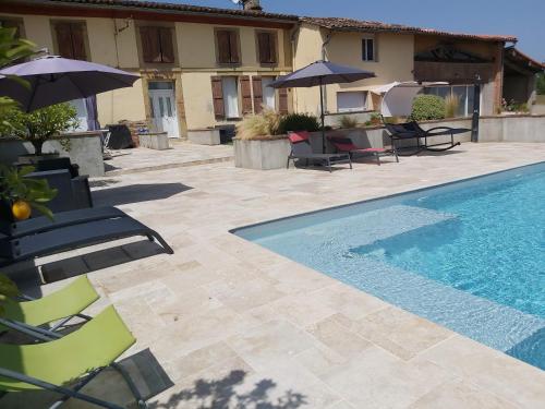 a swimming pool with chairs and umbrellas next to a house at Domaine de Codeval in Fronton